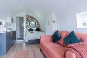 A compact bedroom with a lofted sleeping area, a pink sofa, and a small kitchenette.
