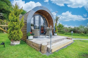 A modern, semi-circular wooden structure with a glass door and a small outdoor seating area with a table and chairs.