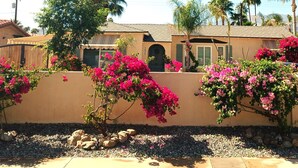 A building with a beige exterior, a number '295' on the wall, and pink bougainvillea plants. - Carrington Cottage @ 420 Shiloh LGBTA Pet friendly Sanctuary with Soul (Palm Springs)