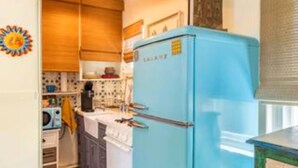 A compact kitchen with a blue refrigerator, white stove, and a tiled floor. - Carrington Cottage @ 420 Shiloh LGBTA Pet friendly Sanctuary with Soul (Palm Springs)