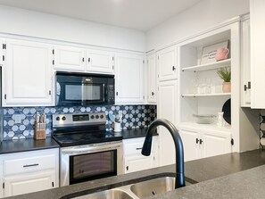 A modern kitchen with white cabinets, a black microwave, a stainless steel oven, and a black faucet. - Trailside Bike-In-Bike-Out Back 40, Hiking Trails, and Golf Course (Bella Vista)