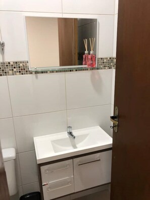 Bathroom features a white sink, mirror, and a shelf with amenities.