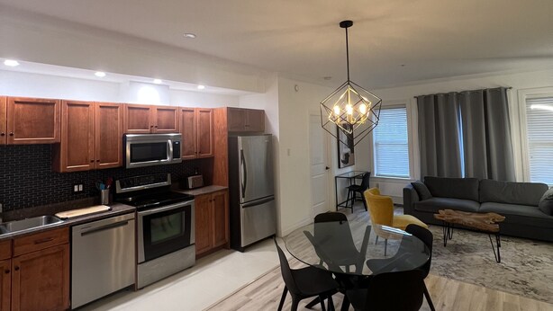 A modern kitchen with stainless steel appliances, wooden cabinets, and a dining area with a glass table and chairs.