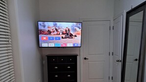 A bedroom with a TV mounted on the wall, a dresser, a door, and a gray rug.