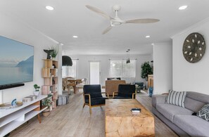 Uma sala de estar moderna com uma TV de tela plana, um ventilador de teto, um sofá e uma mesa de centro.