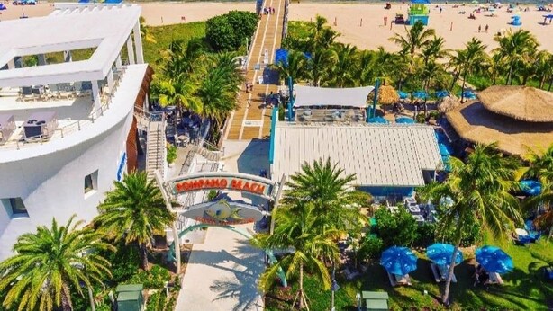 A beach resort with a pier, palm trees, and a pool area. - Private Beach Club, Heated Pool, Jacuzzi, & 6 Seater Golf Cart Included!  (Pompano Beach)