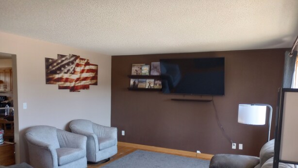 A living room with a sectional sofa, two armchairs, a coffee table, a TV mounted on the wall, and a lamp. - Spacious house with large yard in great location close to boat ramps. (Devils Lake)