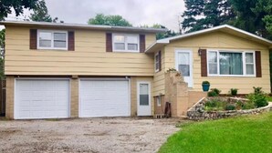A two-story house with two attached garages, a front porch, and a landscaped garden. - Spacious house with large yard in great location close to boat ramps. (Devils Lake)