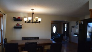 A dining area with a wooden table and chairs, a chandelier, and a refrigerator in the background. - Spacious house with large yard in great location close to boat ramps. (Devils Lake)