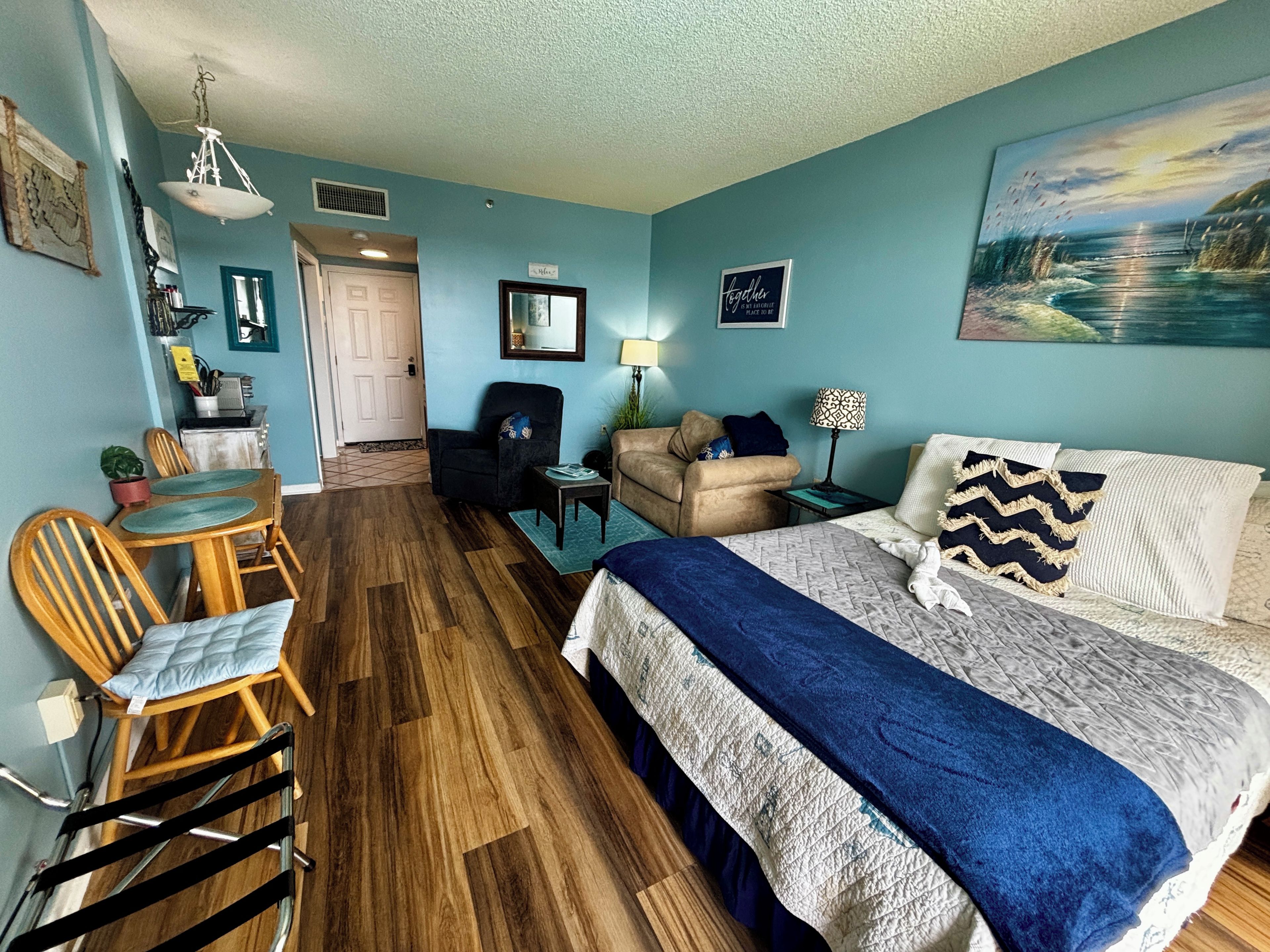 A hotel room with a bed, a desk, a chair, a sofa, and a dining area.