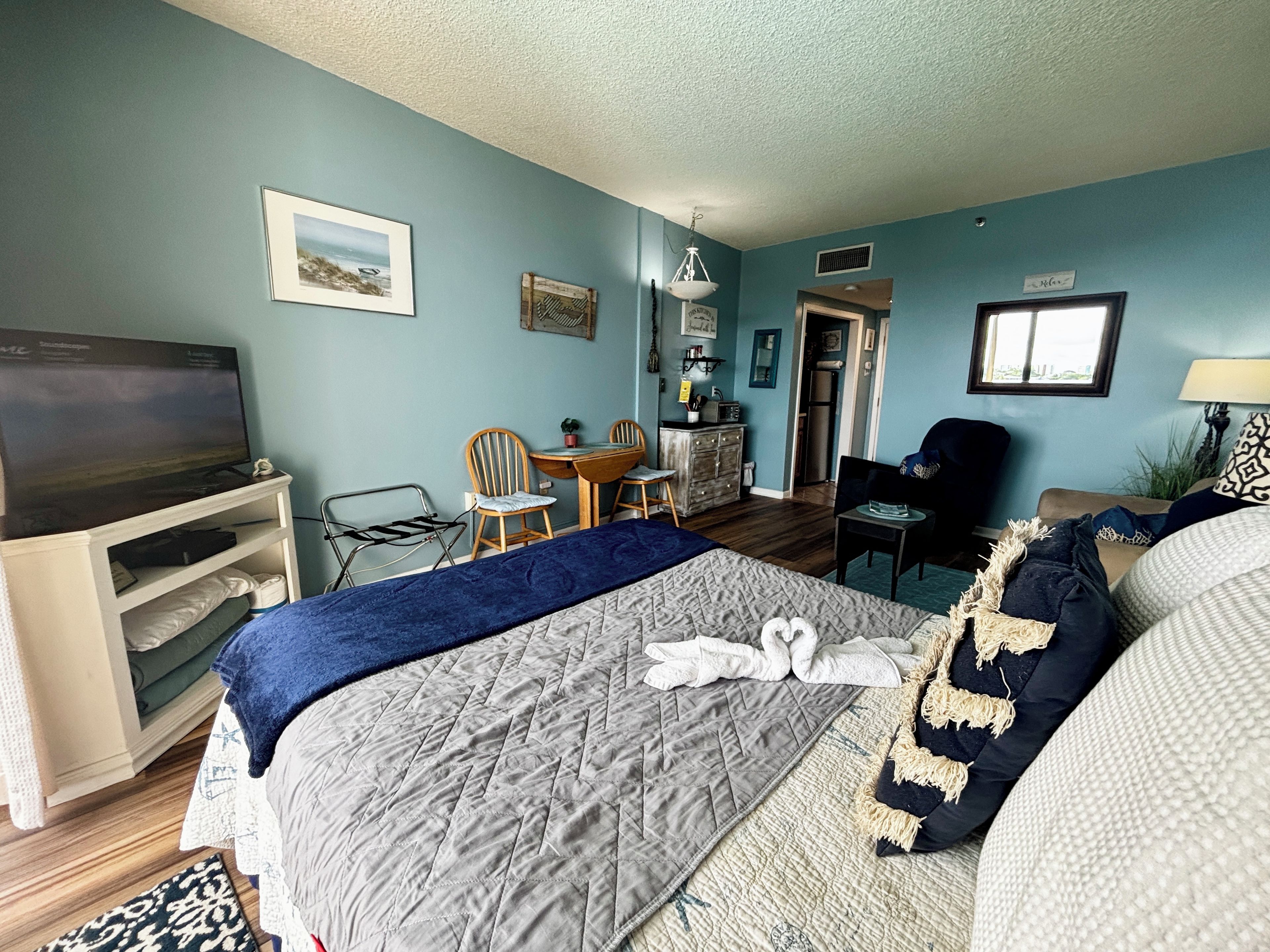 A hotel room with a bed, a television, a desk with a chair, and a kitchenette.