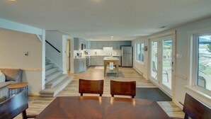 Een ruime woonkamer met een eettafel, twee stoelen, een bank en een keuken op de achtergrond.