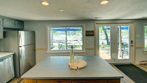 Een keuken met een centraal eiland, een koelkast en uitzicht op de omgeving door een glazen deur.