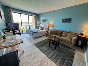 A modern living room with a bed, sofa, and a dining area.