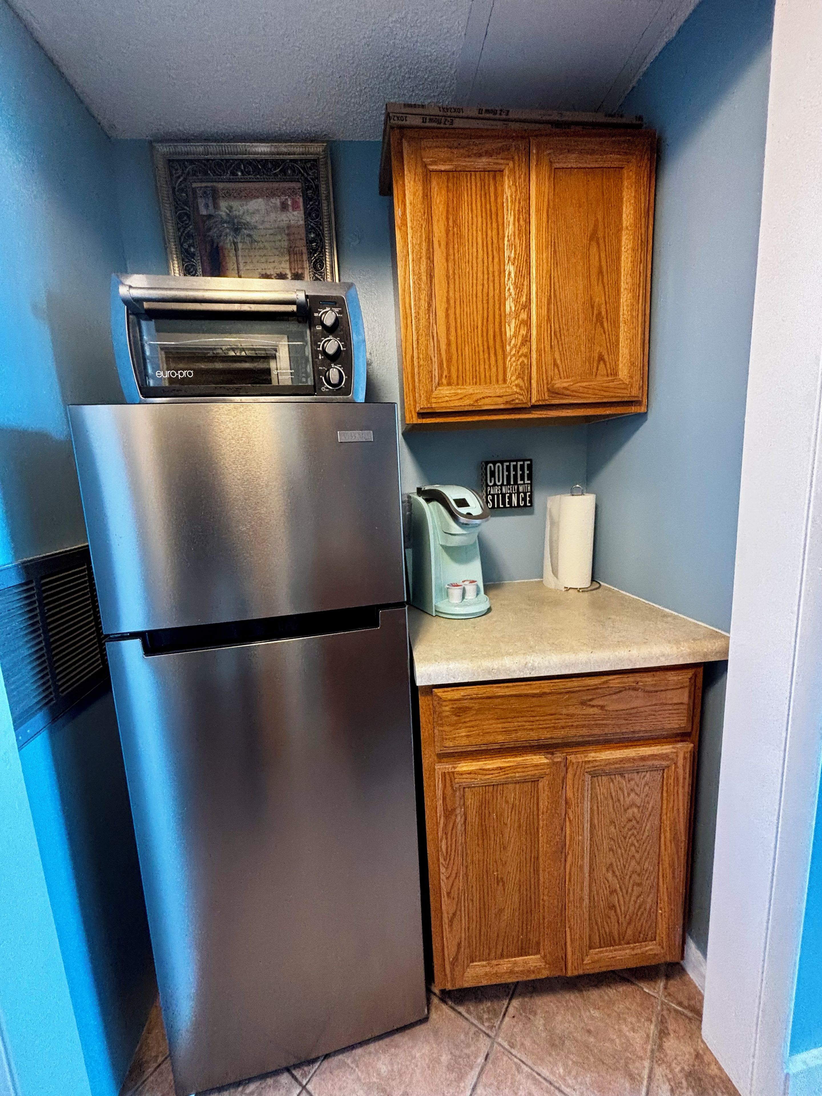 A compact kitchen with a stainless steel refrigerator, a built-in oven, wooden cabinets, and a coffee maker on the countertop.