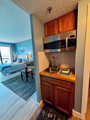 A compact kitchen with wooden cabinets, a stainless steel microwave, and a sink.