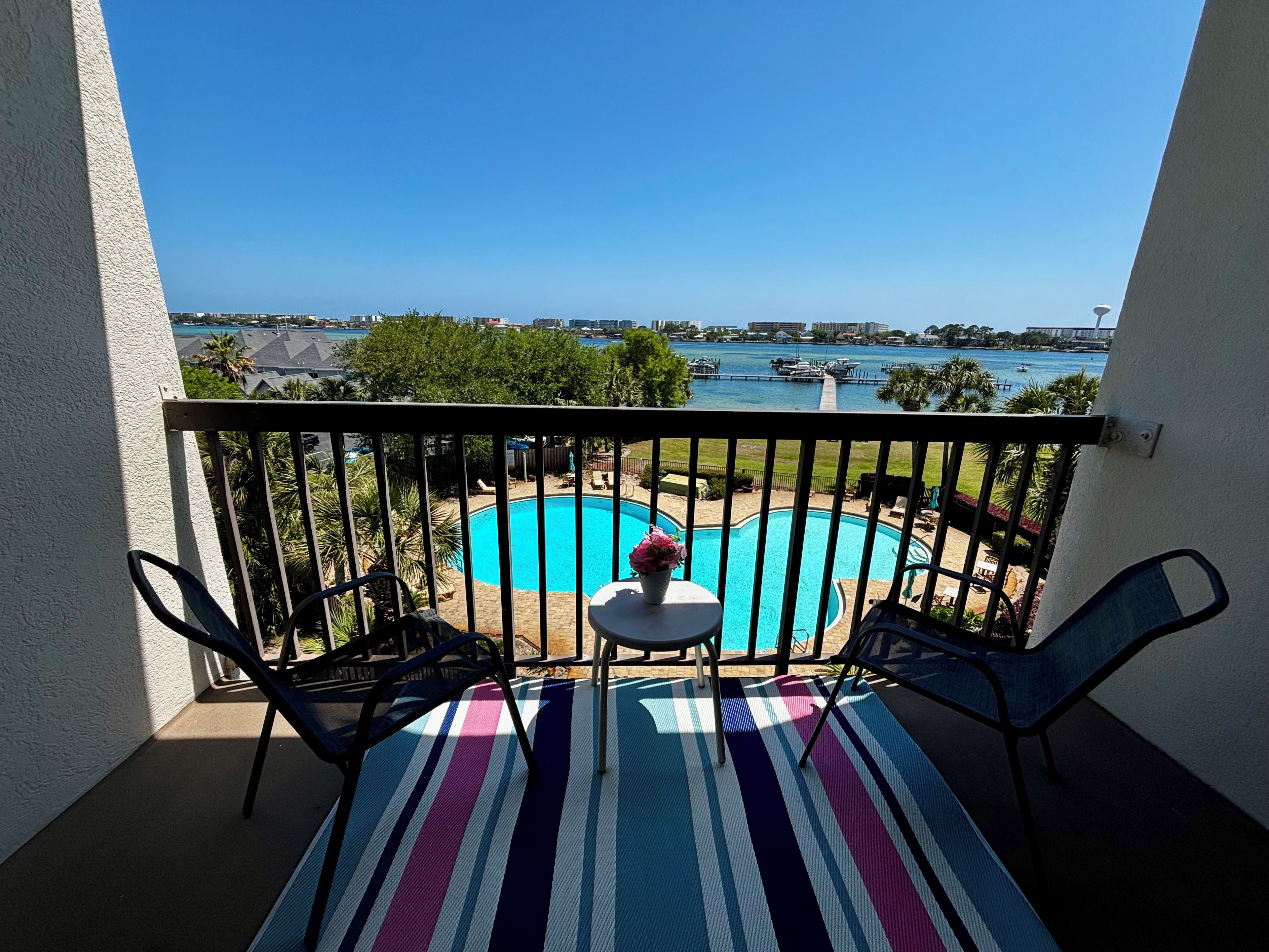 A balcony with a view of a swimming pool, a table with chairs, and a railing.