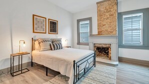 Ein Schlafzimmer mit Bett, Kamin, zwei Fenstern und Deckenventilator.