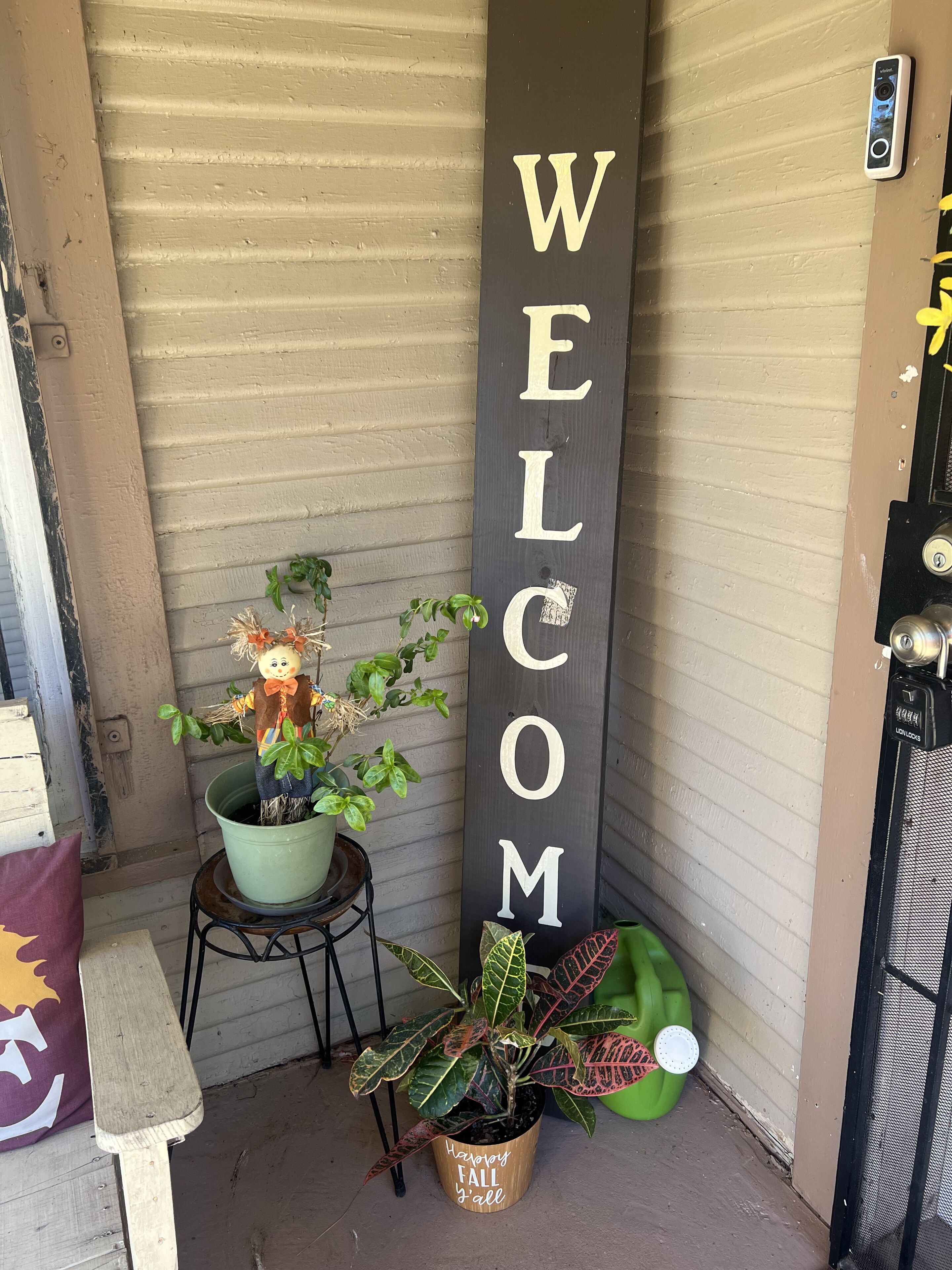 A welcome sign, a potted plant with a scarecrow decoration, and a bench.