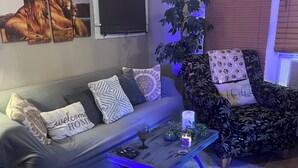 A living room with a grey sofa, a patterned armchair, a coffee table, and a large potted plant. - The Lyons Den - Great work place with high speed internet near downtown.  (Jackson)