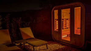 Eine hölzerne Laube mit Glastür, zwei Lounge-Stühlen und einem kleinen Tisch auf einem Kiesgrund.