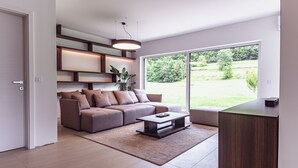 Ein modernes Wohnzimmer mit einer Couch, einem Couchtisch und einem großen Fenster mit Blick ins Freie.