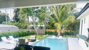A backyard with a swimming pool, lounge chairs, a table, and various plants. - Tropical Oasis!! New Construction! In the Heart of Naples!! PET FRIENDLY! (Naples)