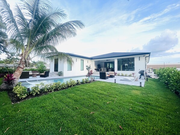 A modern house with a pool, outdoor furniture, and a well-maintained lawn.