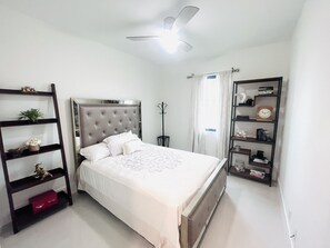 A neatly arranged bedroom with a bed, a bookshelf, a mirror, and a ceiling fan.