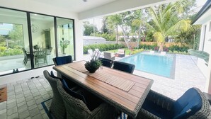 A modern outdoor dining area with a pool, wicker furniture, and a ceiling fan. - Tropical Oasis!! New Construction! In the Heart of Naples!! PET FRIENDLY! (Naples)