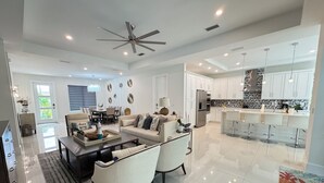 A modern living room with a sofa, coffee table, and chairs. There is a dining area with a table and chairs, and a kitchen with white cabinets and a bar. - Tropical Oasis!! New Construction! In the Heart of Naples!! PET FRIENDLY! (Naples)