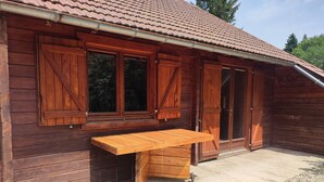 A wooden cabin with a large sliding door, a window with shutters, and a wooden table outside. - Chalet au Coeur de la Nature (Cerniébaud)