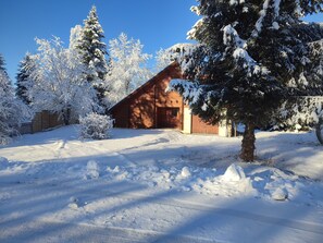 Eine Holzhütte in einer schneebedeckten Landschaft, umgeben von Bäumen.