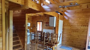 A wooden cabin interior with a dining area, kitchen, and a loft bedroom. - Chalet au Coeur de la Nature (Cerniébaud)