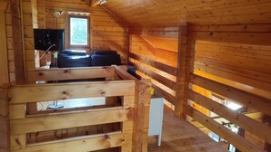 A wooden cabin interior with a loft bed, a sofa, and a television. - Chalet au Coeur de la Nature (Cerniébaud)