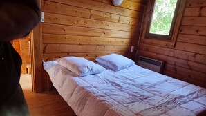 A wooden cabin room with a bed, pillows, and a window. - Chalet au Coeur de la Nature (Cerniébaud)