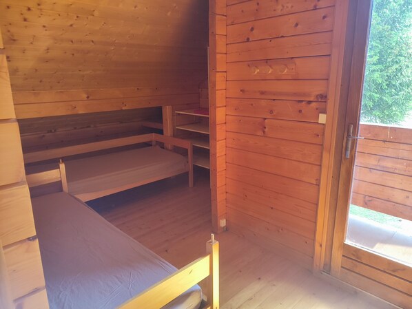 A wooden cabin interior with a bunk bed, a small table, and a window.