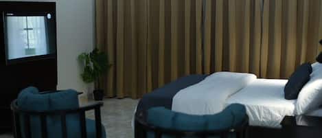 A hotel room with a bed, two chairs, a TV, and a curtain.