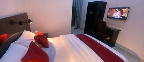Una habitación de hotel con cama, televisor montado en la pared y escritorio con silla.