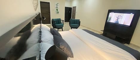 A hotel room with a bed, two chairs, a television, and a door.