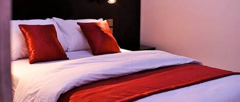 A neatly made bed with white and red bedding, a dark headboard, and a wall-mounted light fixture.