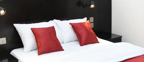 A neatly made bed with white and red pillows, a black nightstand with a lamp, and a black headboard.
