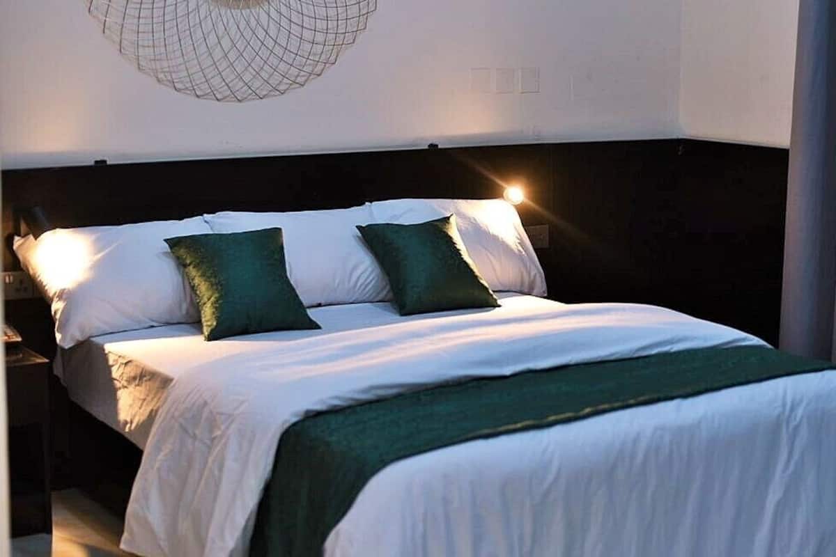 A neatly made bed with white and green bedding, a dark headboard, and a wall-mounted light fixture.
