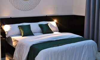 Una cama bien hecha con ropa de cama blanca y verde, un cabecero oscuro y una lámpara fijada a la pared.