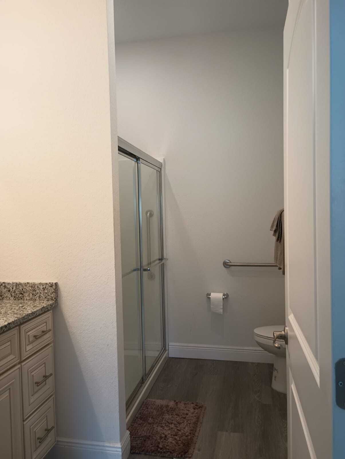 A bathroom with a glass shower enclosure, a toilet, and a granite countertop with drawers.
