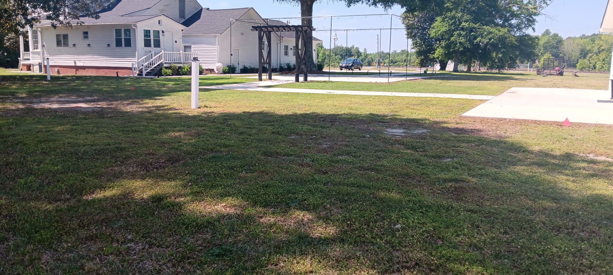 A grassy yard with a house, a pergola, and a fence.