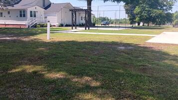 A grassy yard with a house, a pergola, and a fence.
