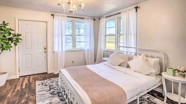 Un dormitorio con cama, candelabro, ventana con cortinas, puerta y una planta en maceta.