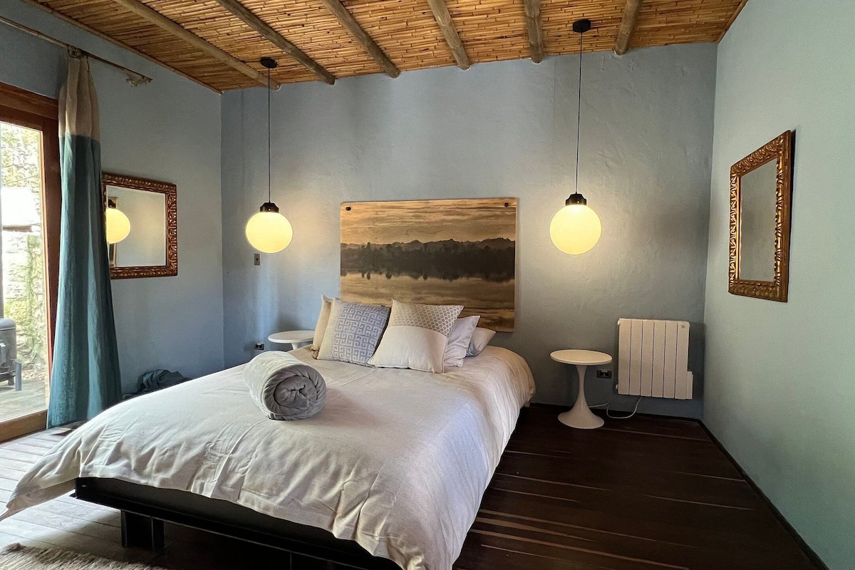 A bedroom with a bed, bedside tables, a radiator, and a large painting on the wall.