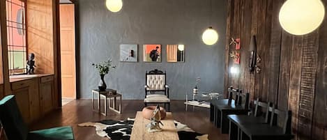 A spacious room with a high ceiling, wooden beams, a cowhide rug, a dining table with chairs, and pendant lighting.